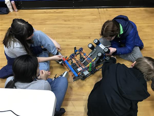 Students sit around and work on their robot at a VEX IQ Robotics competition.